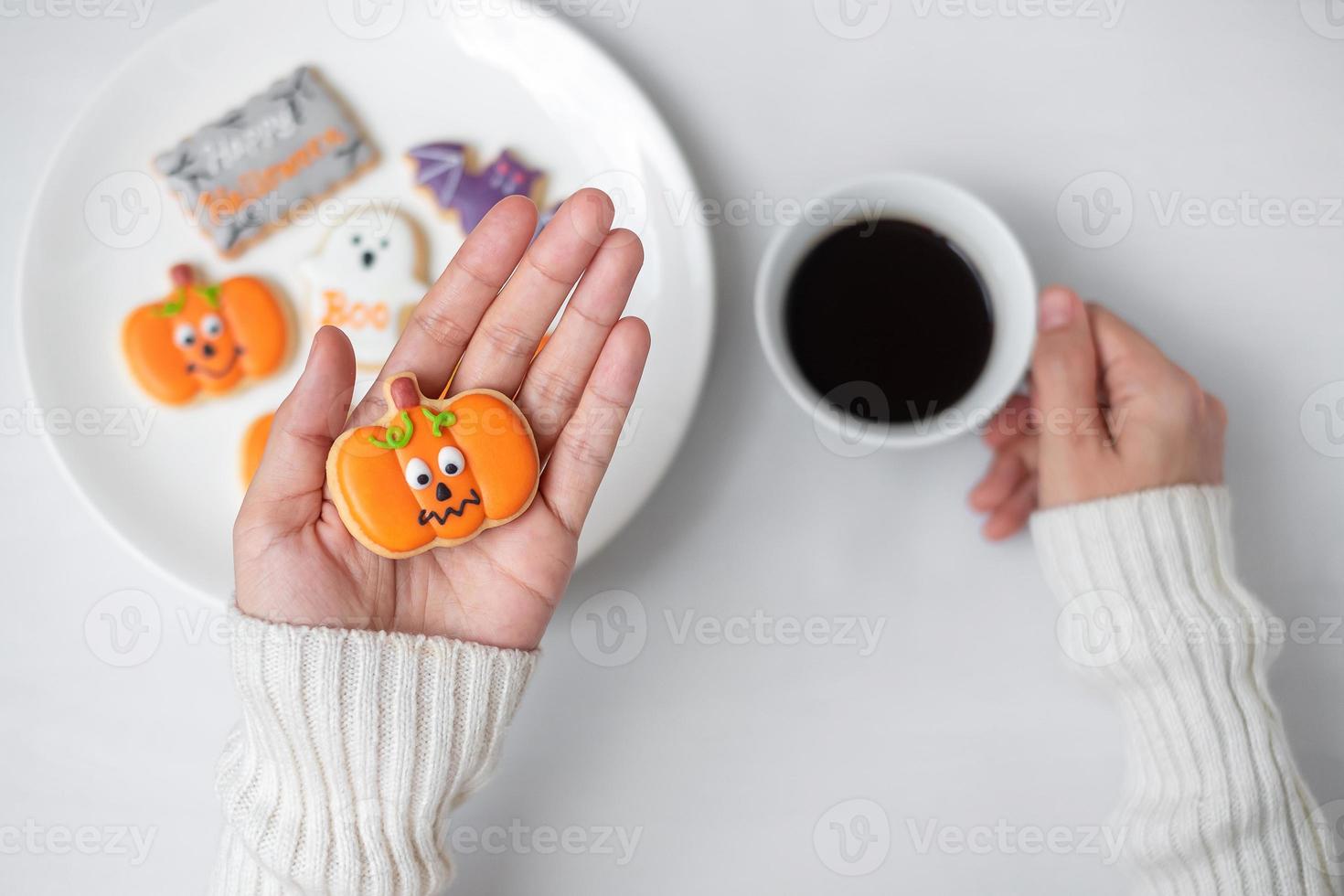 mão de mulher segurando biscoito engraçado de halloween durante a beber café. feliz dia das bruxas, truque ou ameaça, olá outubro, outono outono, conceito tradicional, festa e feriado foto