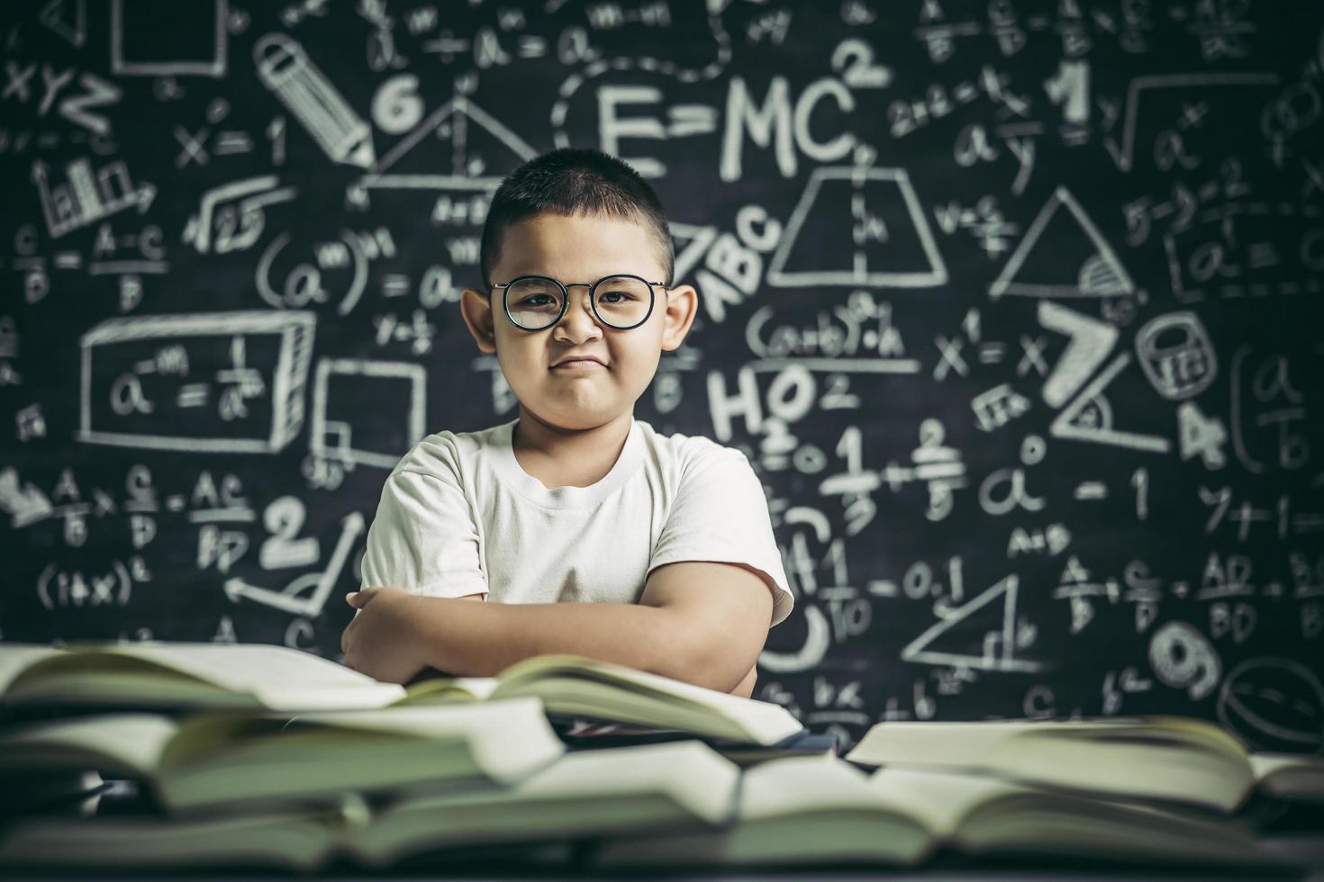 um menino de óculos sentado na sala de aula lendo foto