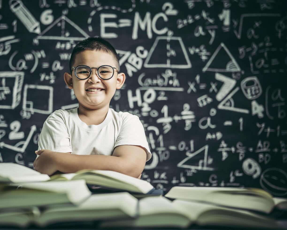 um menino de óculos sentado na sala de aula lendo foto