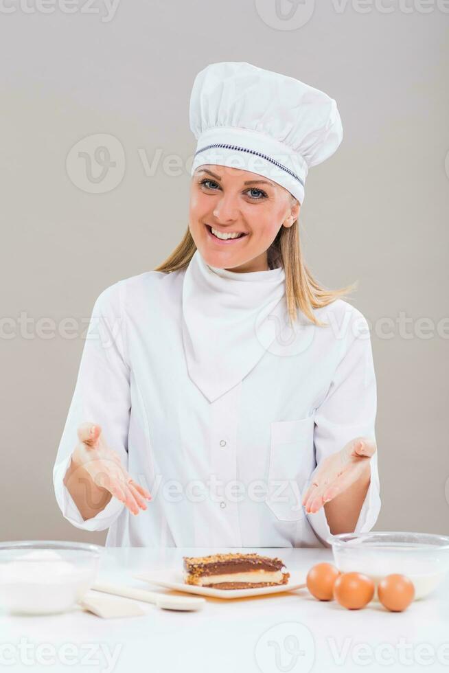 lindo fêmea pasteleiro é mostrando fatia do bolo enquanto sentado às a mesa foto