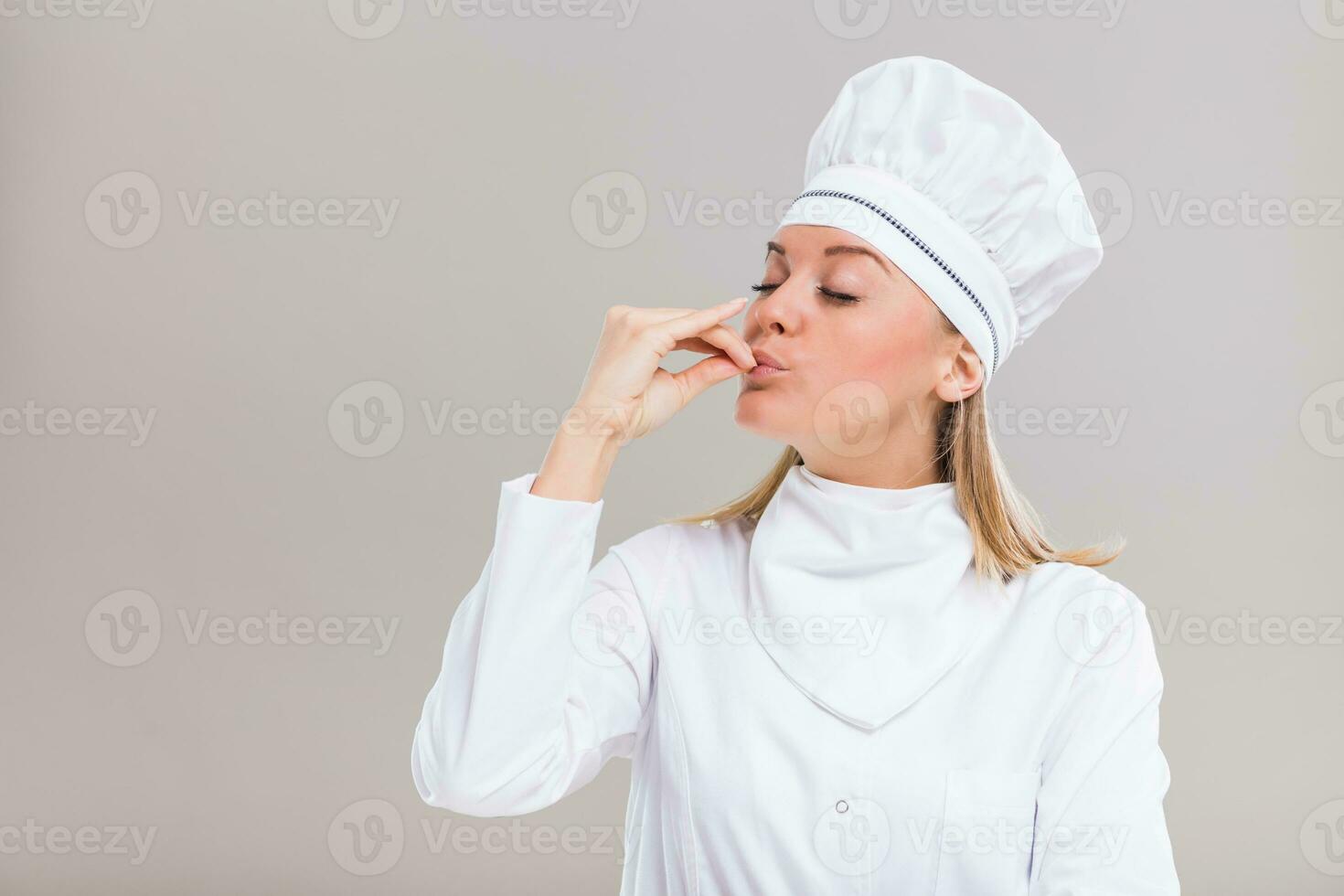lindo fêmea chefe de cozinha é mostrando delicioso placa em cinzento fundo. foto