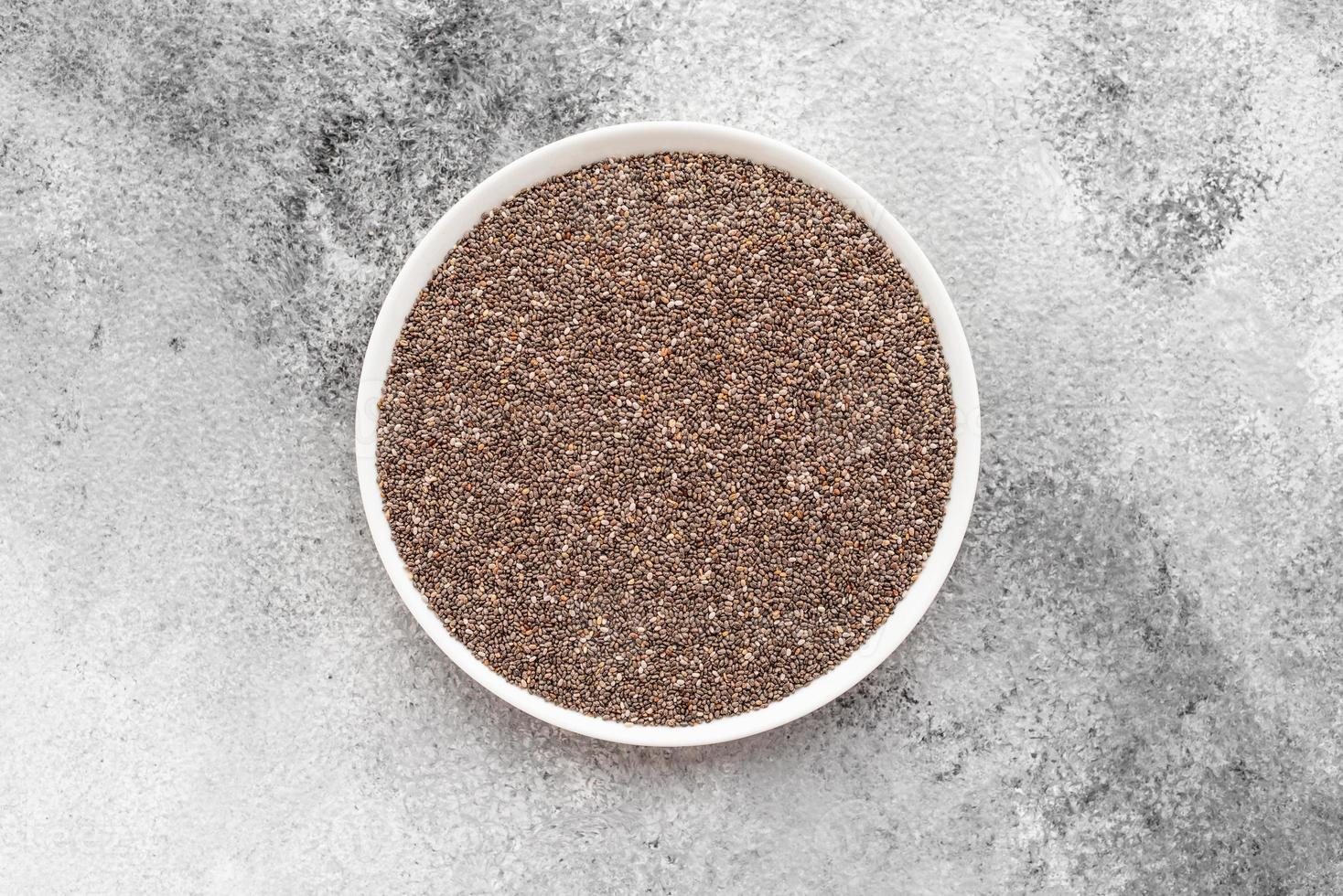 sementes de chia em um pires branco sobre um fundo cinza de concreto foto