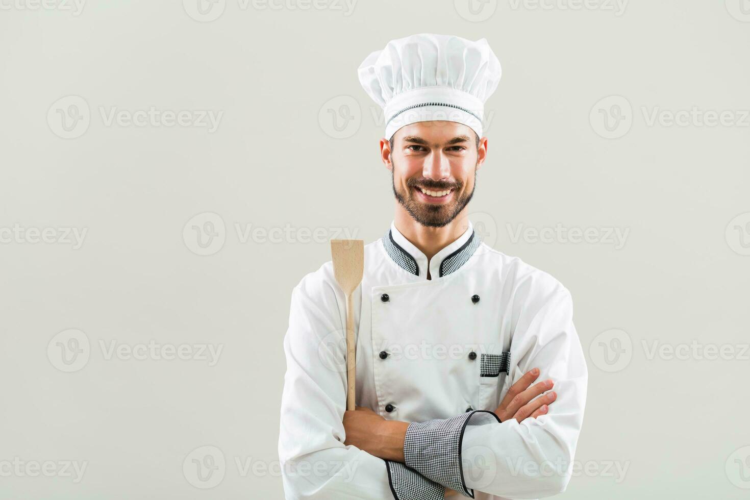 retrato do sorridente chefe de cozinha segurando de madeira colher em cinzento fundo. foto