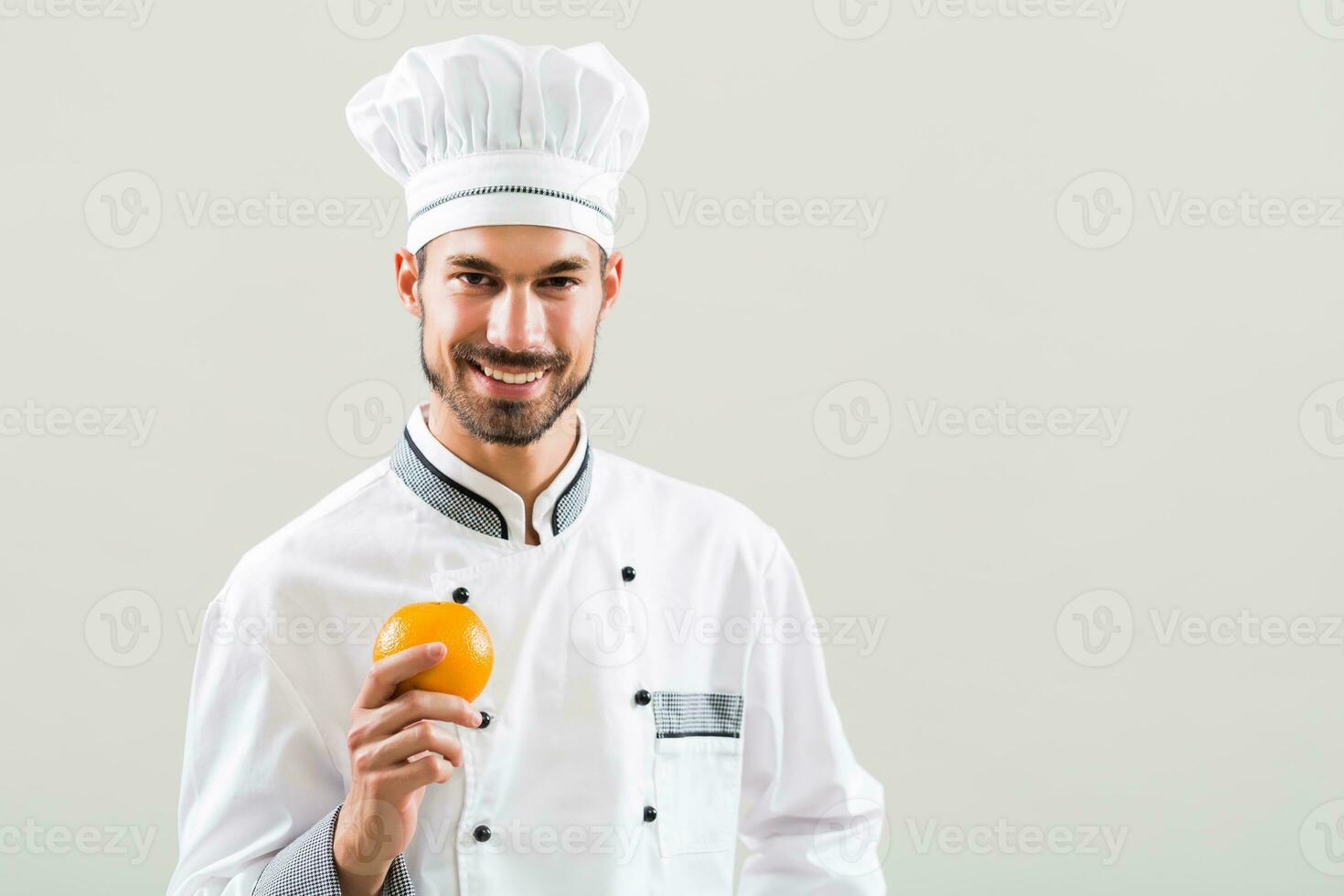 chefe de cozinha é segurando laranja em cinzento fundo. foto