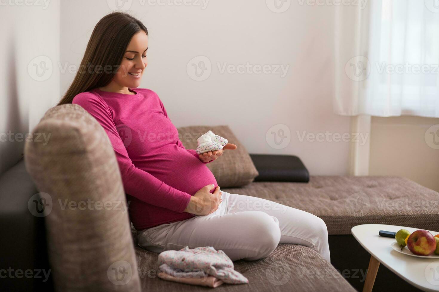 feliz grávida mulher segurando pequeno bebê meias. foto