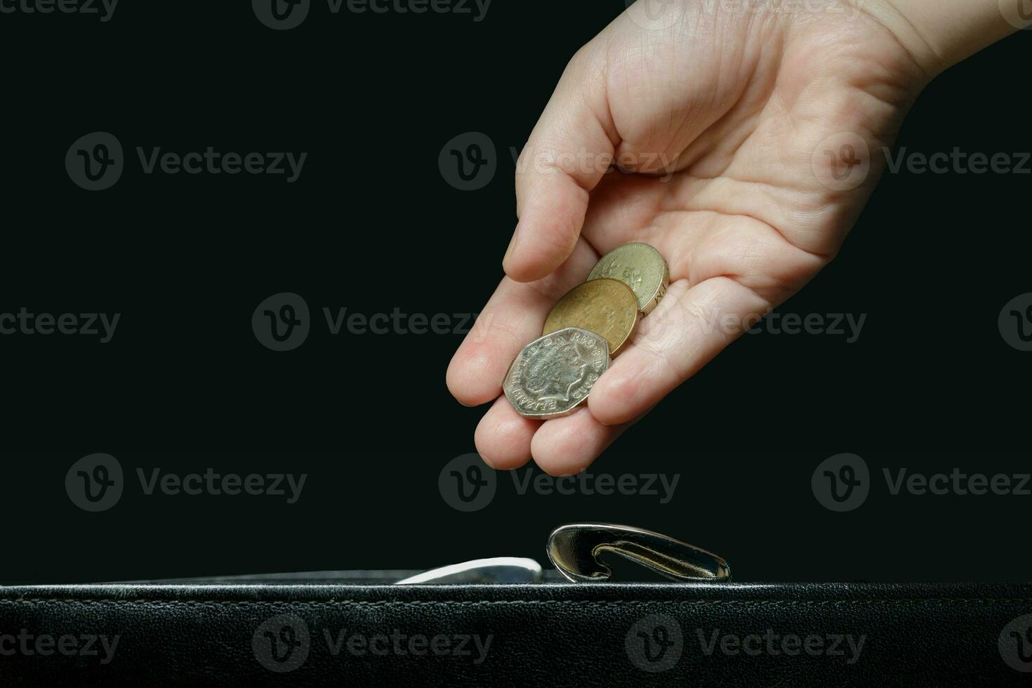 a invisível mulher mão coloca uma moedas dentro uma carteira.a Preto fundo foto