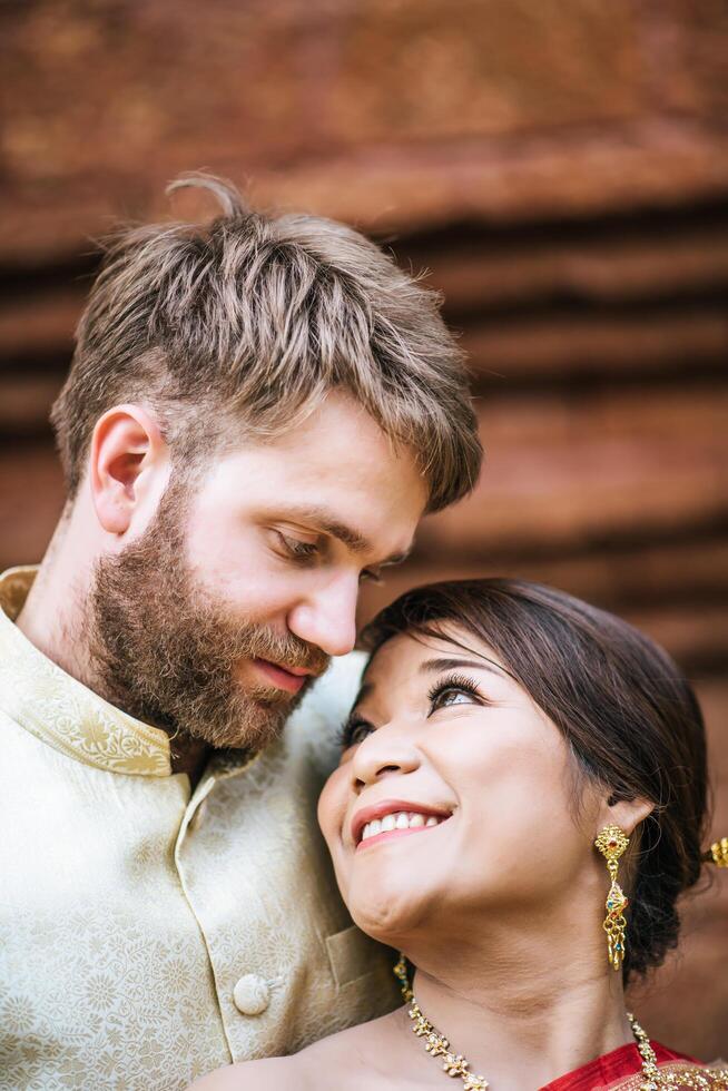 Noiva asiática e noivo caucasiano se divertindo com um vestido tailandês foto