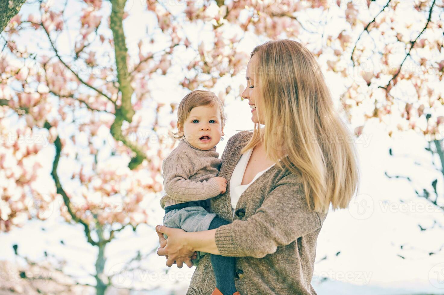 ao ar livre retrato do feliz jovem mãe com adorável bebê menina debaixo florescendo Primavera árvore, inferior Visão foto