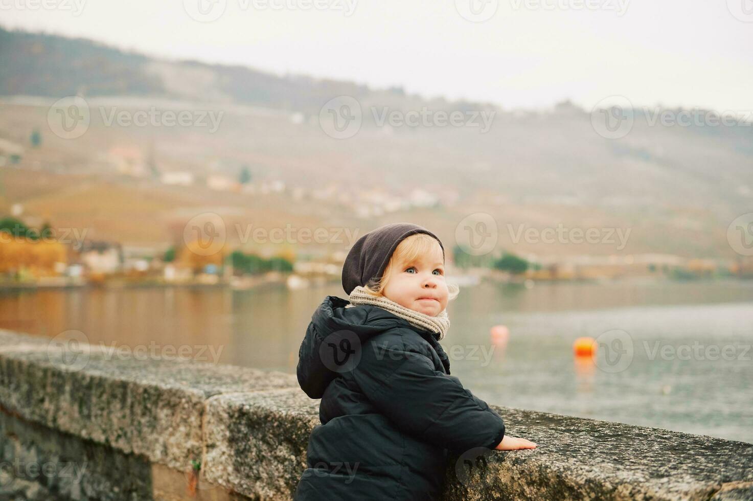 ao ar livre retrato do adorável criança pequena menina jogando de a lago em uma frio outono dia, vestindo caloroso Jaqueta e chapéu foto