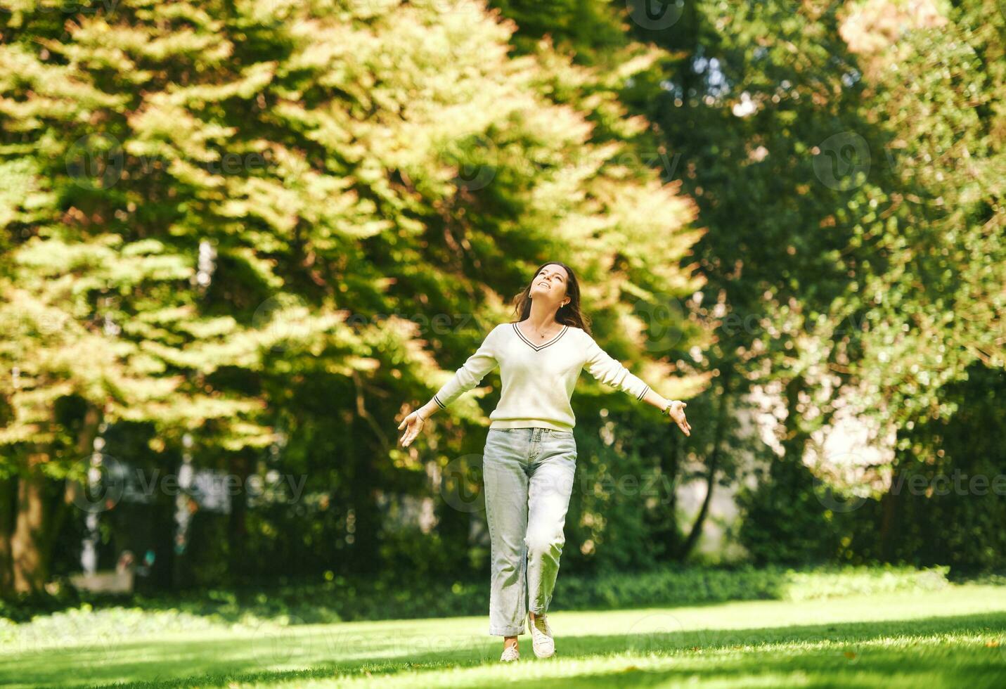 ao ar livre retrato do feliz e saudável 40. - 45 ano velho mulher desfrutando agradável ensolarado dia dentro parque, braços Largo aberto foto
