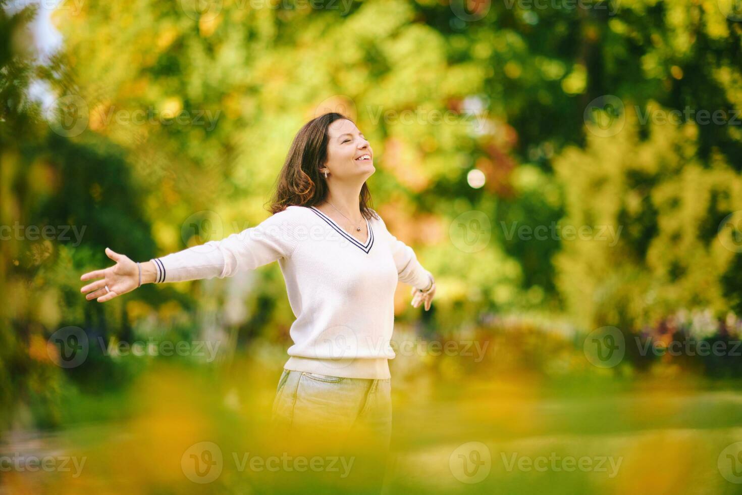 ao ar livre retrato do feliz e saudável 40. - 45 ano velho mulher desfrutando agradável ensolarado dia dentro parque, braços Largo aberto foto