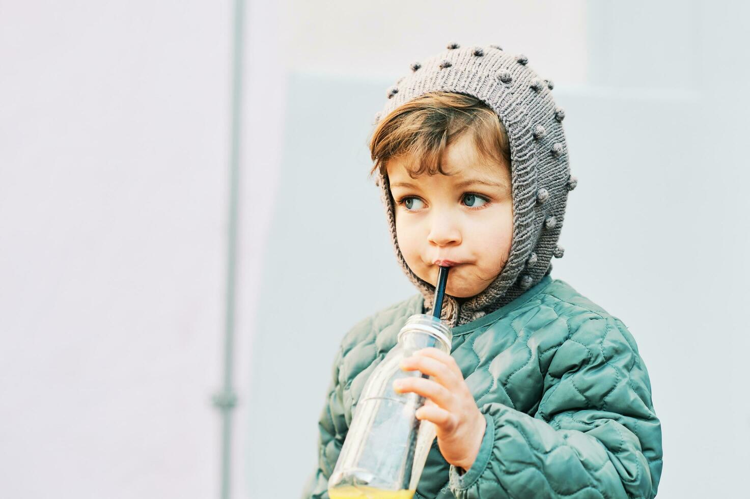 ao ar livre retrato do fofa pequeno menina bebendo suco a partir de garrafa, vestindo caloroso Jaqueta foto