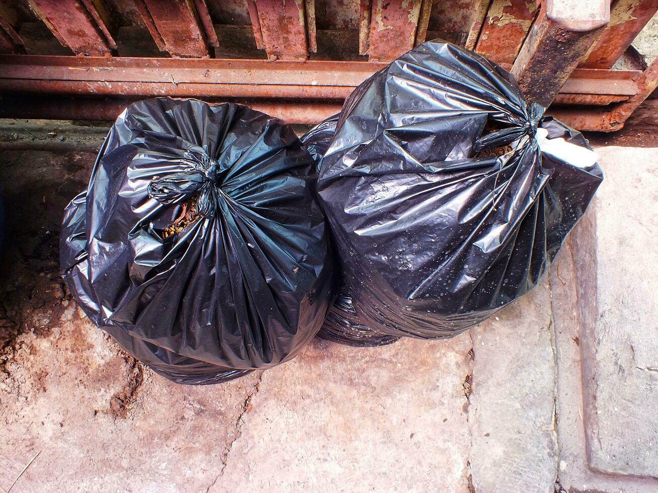 Preto plástico bolsas do lixo pilha ao lado a velho oxidado francês. pilha do Preto lixo em a trilha às lado estrada dentro grande cidade, poluição Lixo foto