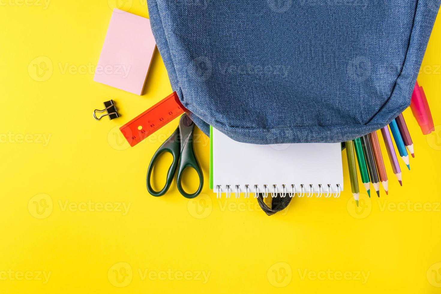 mochila escolar com material de escritório em fundo amarelo. lugar para texto. foto