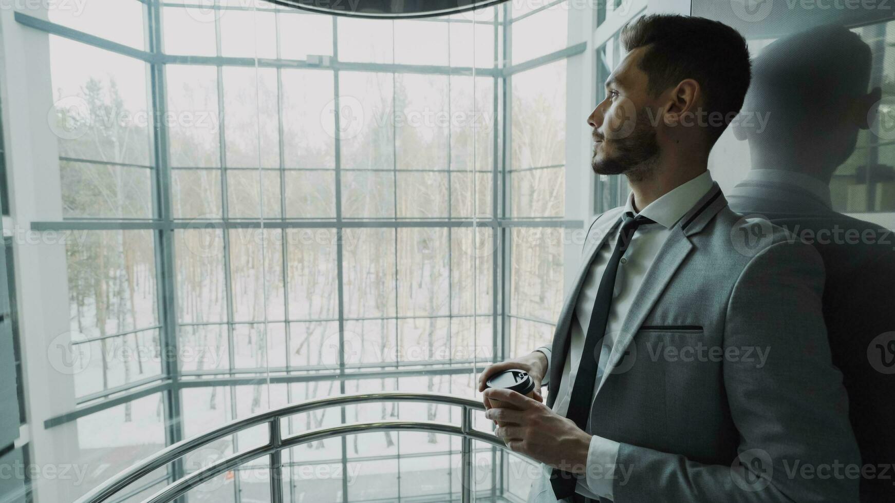 jovem bonito homem de negocios dentro terno bebendo café comovente acima dentro elevador dentro moderno o negócio Centro dentro de casa foto