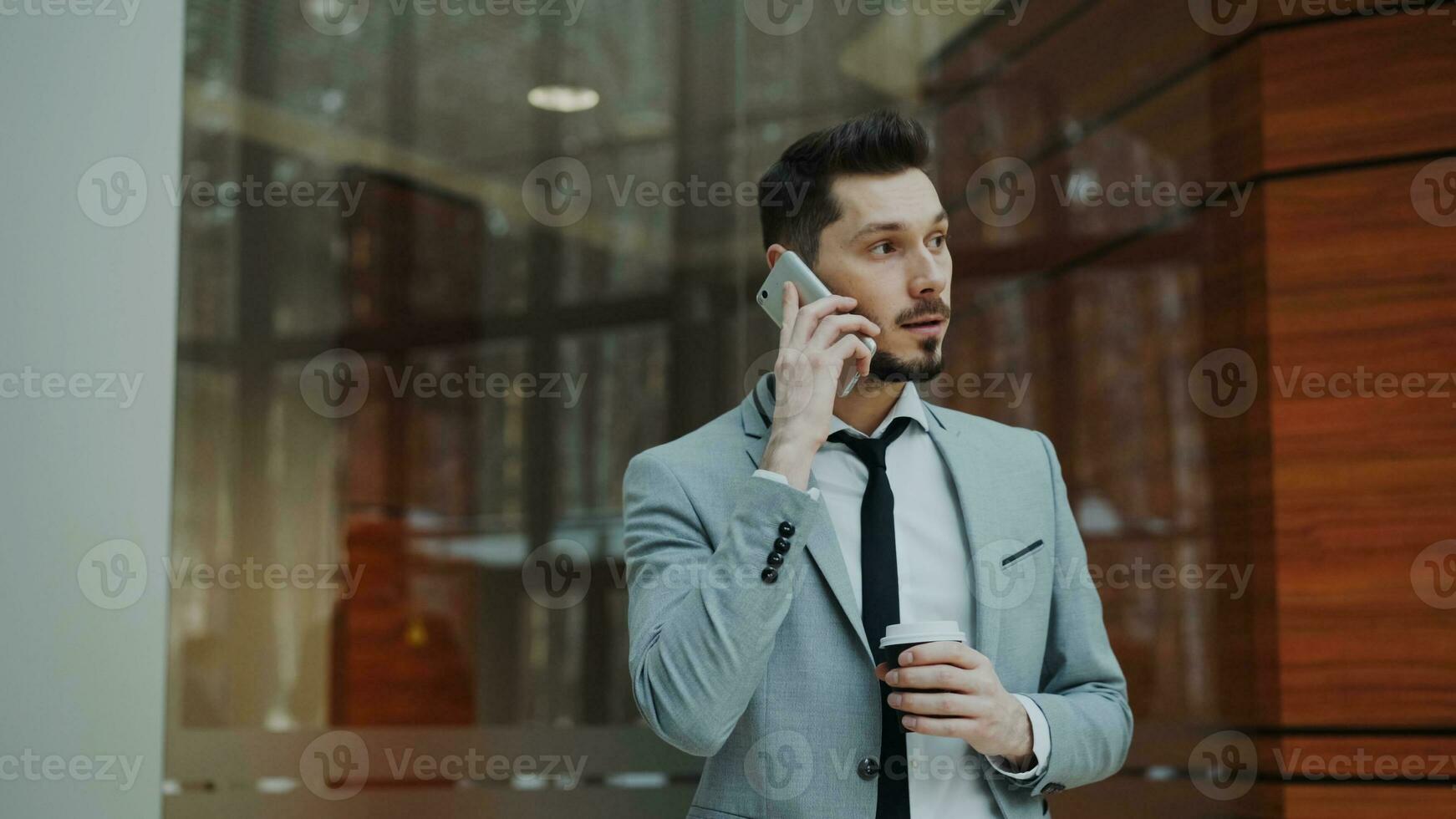 Stedicam tiro do alegre homem de negocios falando com Smartphone e caminhando dentro moderno escritório corredor dentro de casa foto