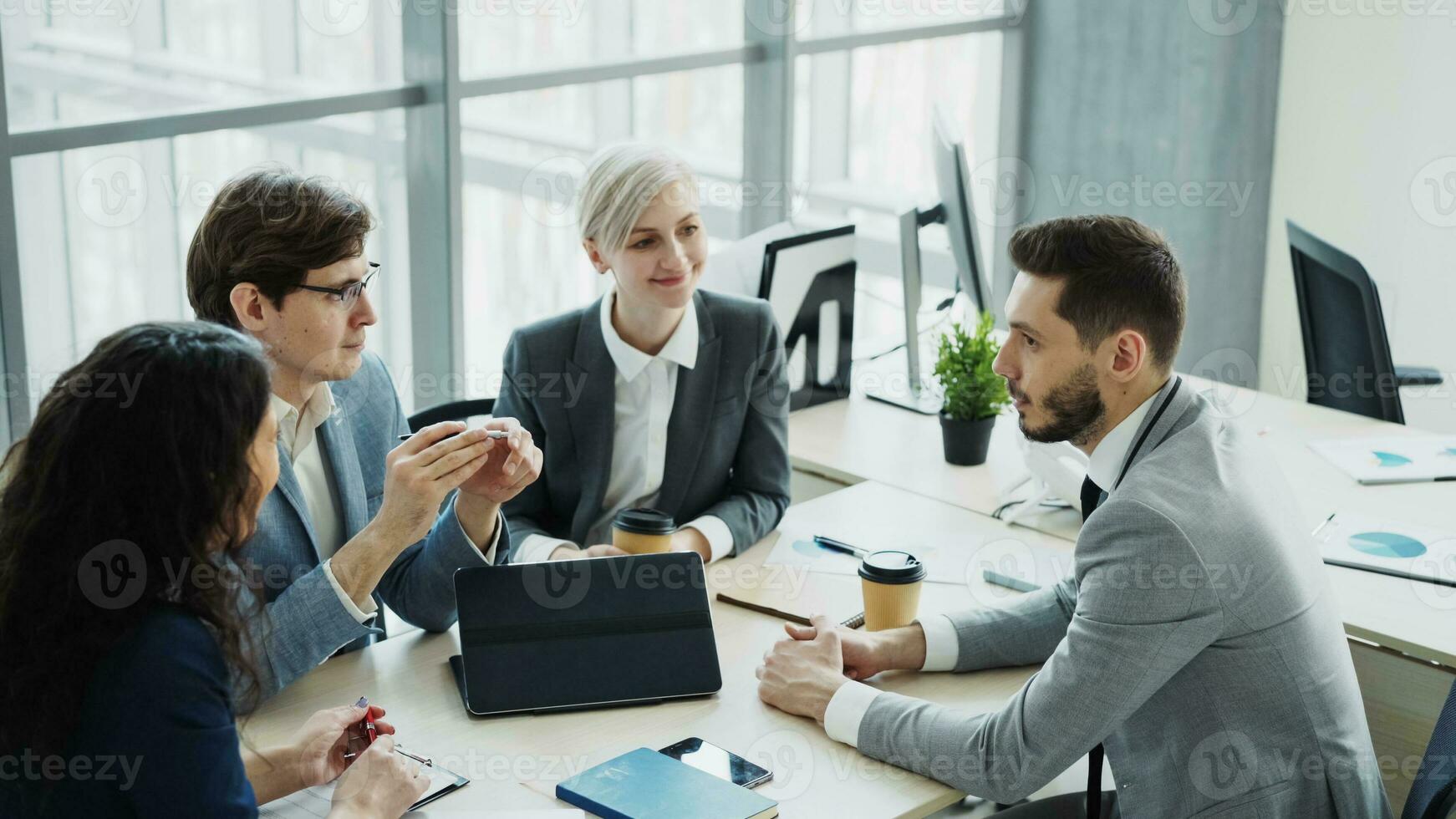 homem de negocios discutindo futuro o negócio projeto com masculino e fêmea colegas sentado às a mesa dentro moderno escritório dentro de casa foto