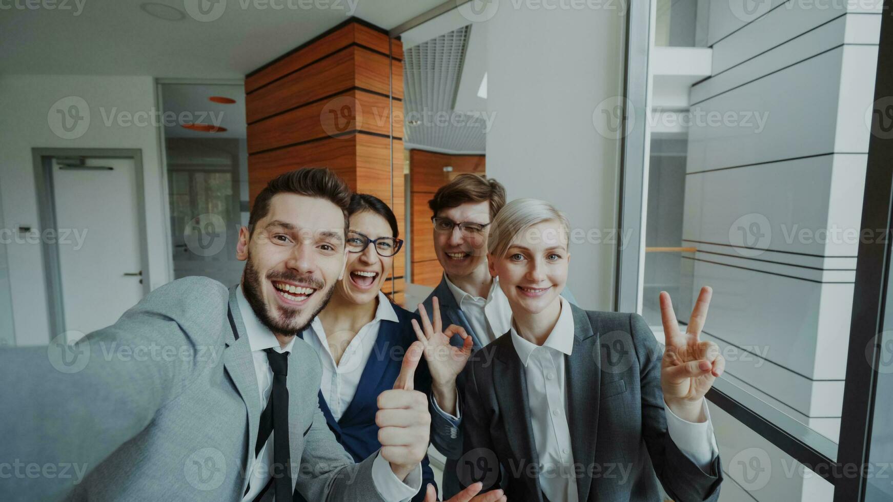 pov do feliz o negócio equipe levando selfie retrato em Smartphone Câmera e posando para grupo foto durante encontro dentro moderno escritório dentro de casa