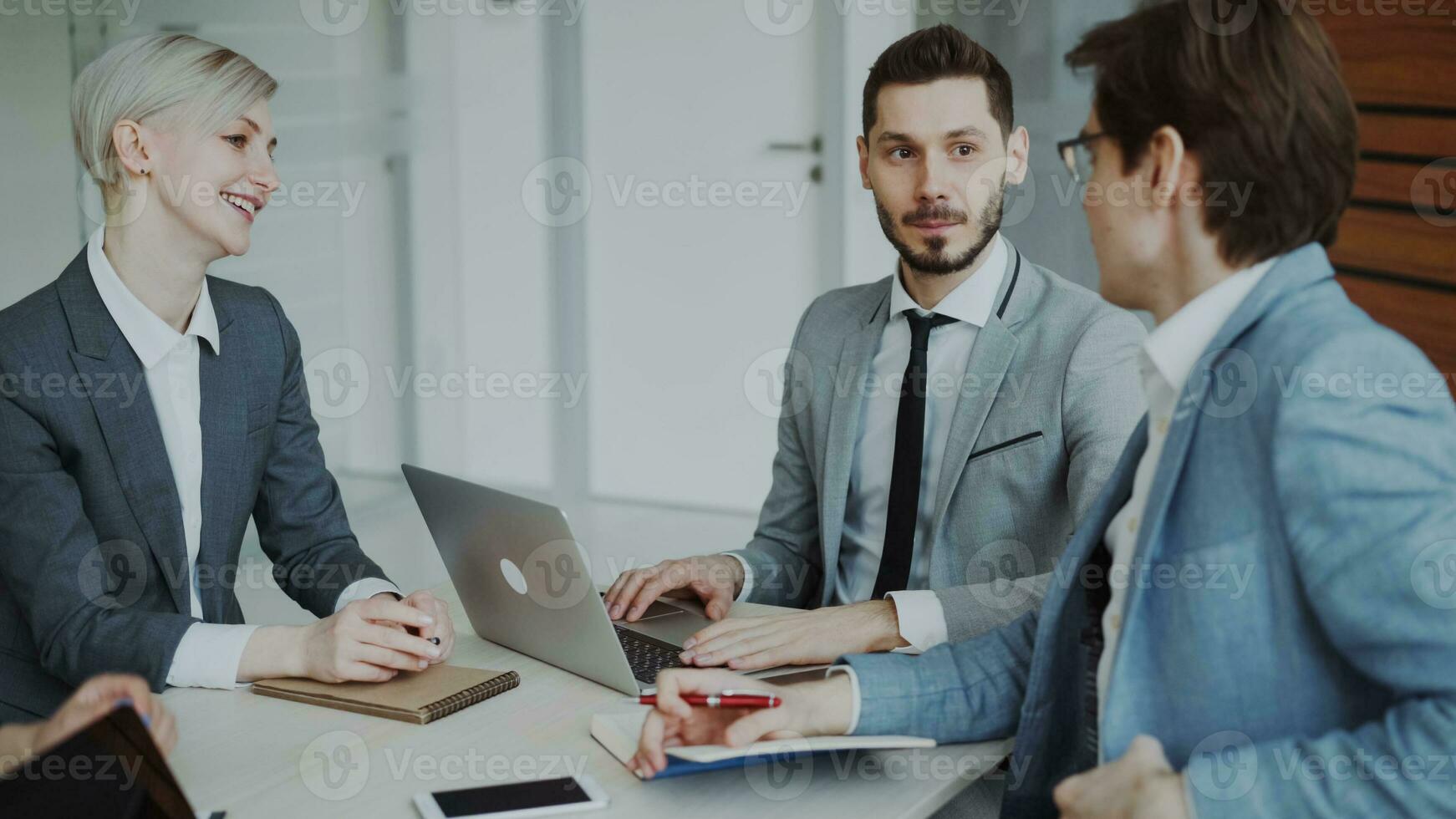 homem de negocios discutindo futuro o negócio projeto com masculino e fêmea colegas sentado às a mesa dentro moderno escritório dentro de casa foto