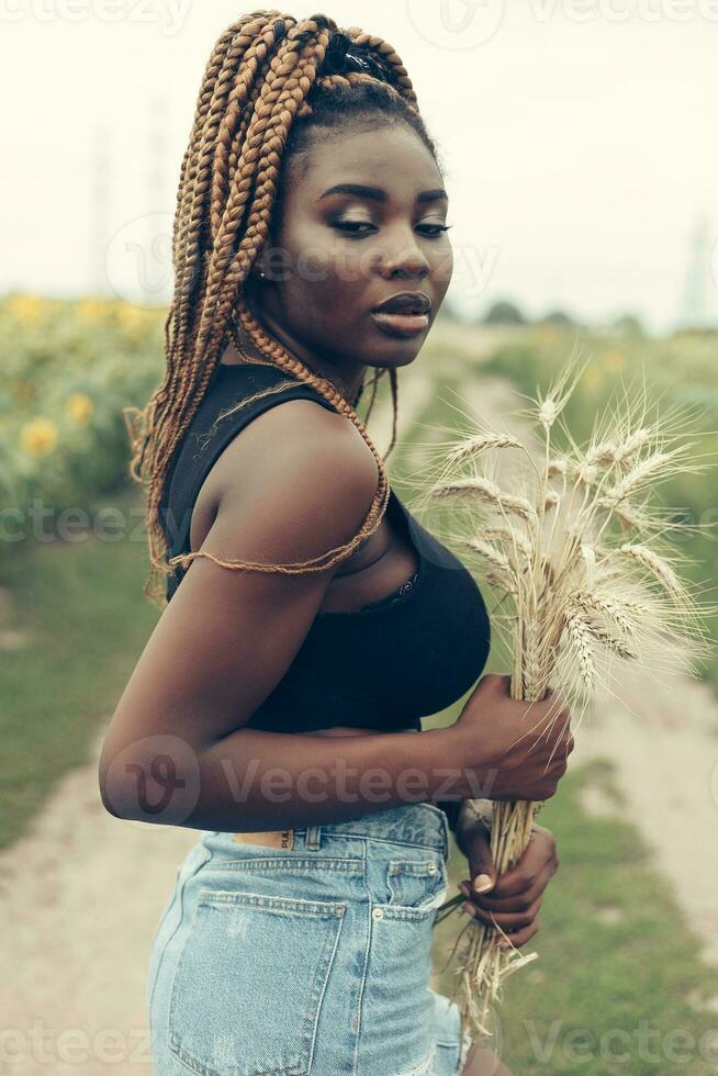 africano americano menina dentro uma campo do amarelo flores às pôr do sol foto