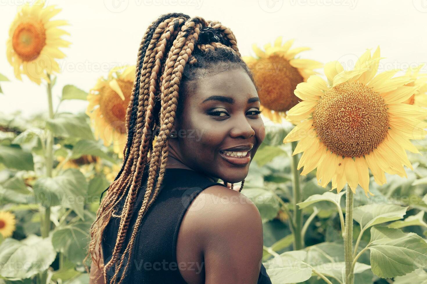 africano americano menina dentro uma campo do amarelo flores às pôr do sol foto