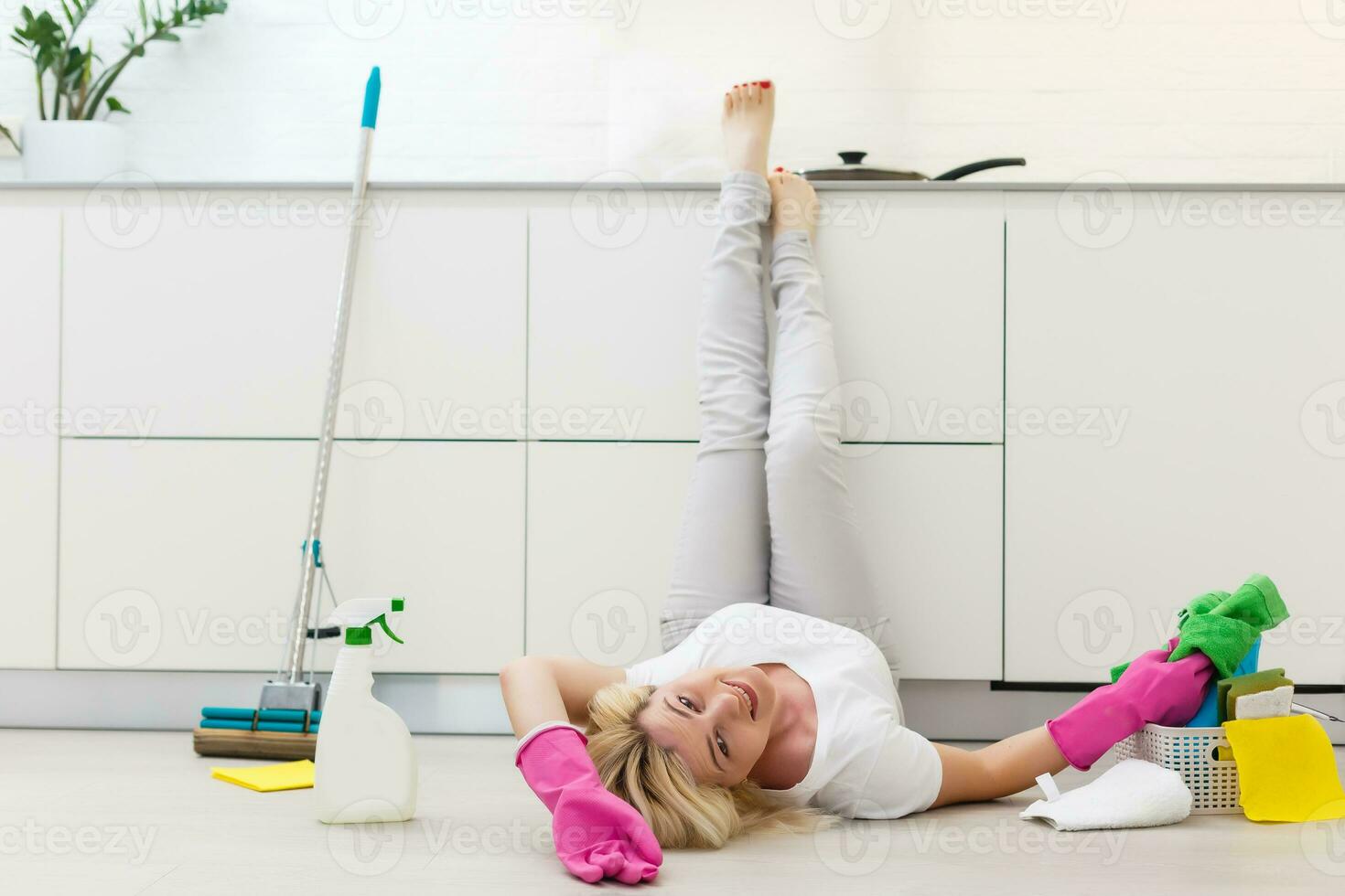 dona de casa ajoelhado baixa em a de madeira chão segurando pano vestindo luvas e avental em repouso. Exausta mulher cansado depois de fazendo tarefas domésticas preparado Novo ano feriados. limpeza produtos dentro balde foto