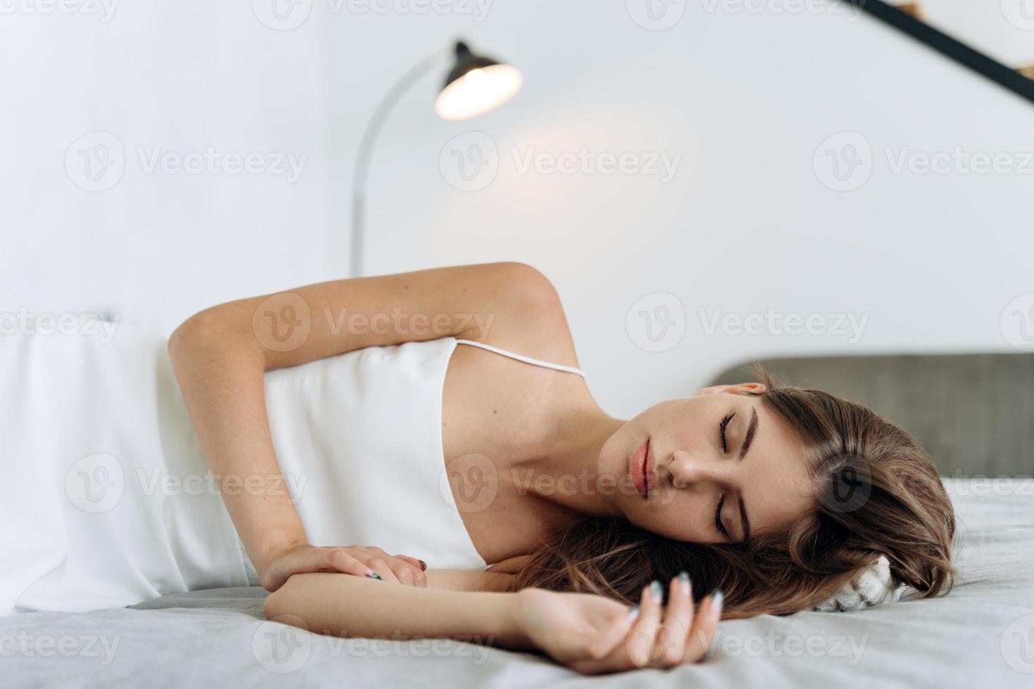 mulher dormindo. bela jovem com cabelos longos, deitada na cama e mantendo os olhos fechados enquanto dormia pela manhã. estilo de vida das pessoas e conceito de aparência feminina foto