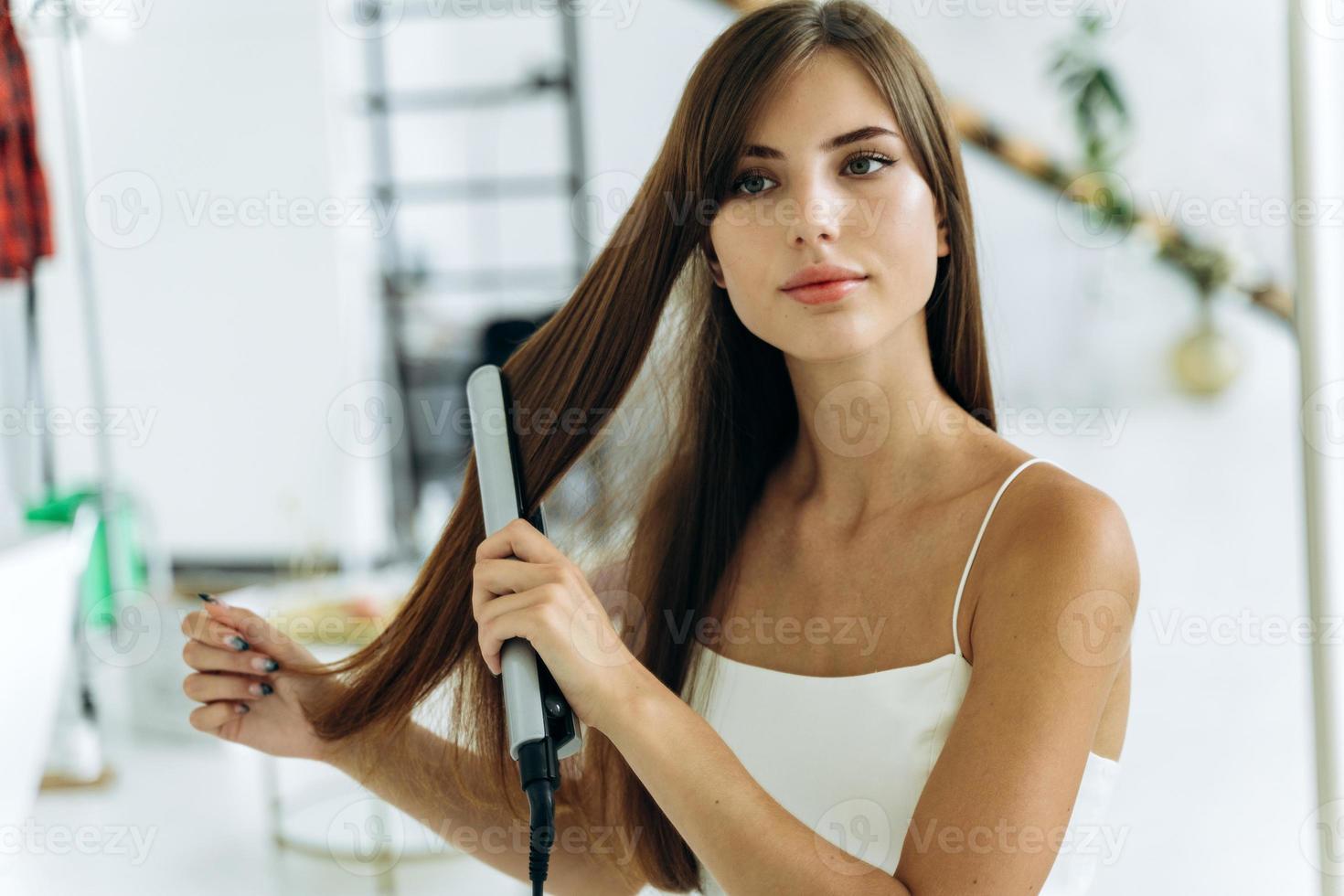 novo estilo de cabelo. jovem alegre se sentindo confiante e sorridente, segurando um lisonjeiro ferro e alisando seu cabelo saudável foto