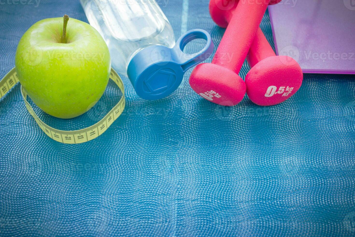dois vermelho halteres, a maçã, uma fita medir, uma garrafa do água e peso balanças em uma ioga esteira. conceitos sobre fitness, esporte e saúde foto