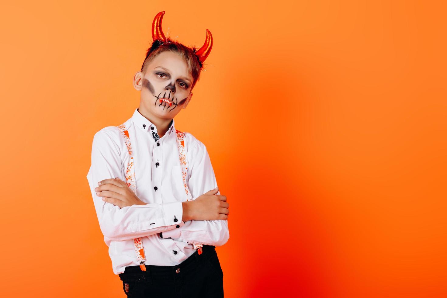 retrato de menino em diabo mascarada maquiagem mãos postas e olhando para a câmera. conceito de halloween foto