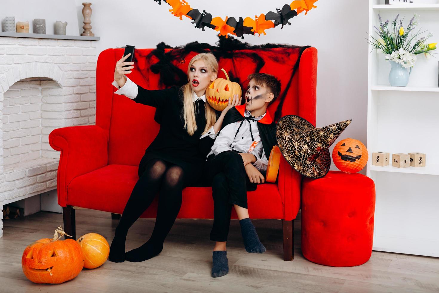 mulher e filho se divertem no sofá vermelho e fazem uma selfie. emoção e conceito de halloween foto