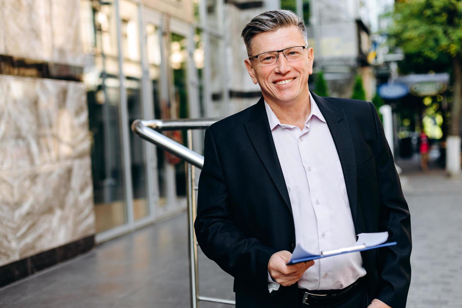 sorridente empresário sênior de óculos segurando um documento e olhando para a câmera - imagem foto