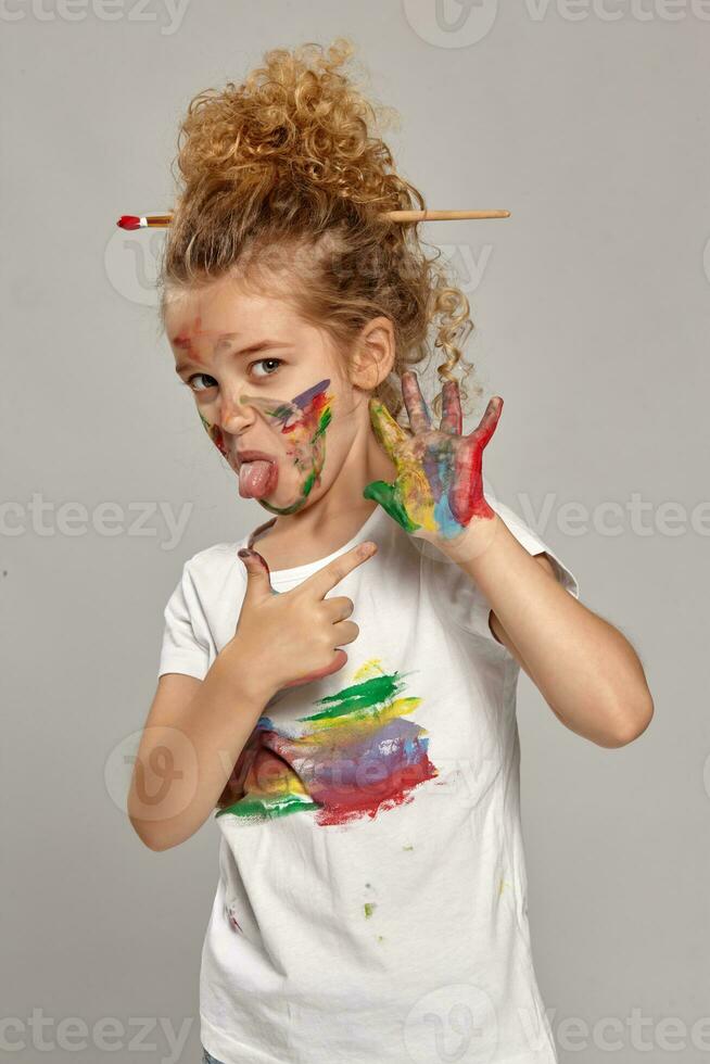 lindo pequeno menina com uma pintado mãos e bochechas é posando em uma cinzento fundo. foto