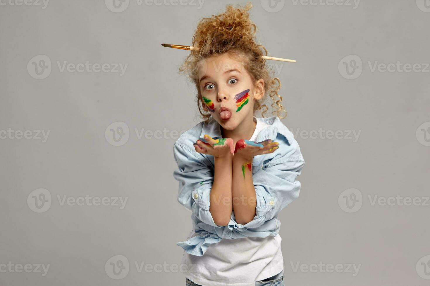 lindo pequeno menina com uma pintado mãos e bochechas é posando em uma cinzento fundo. foto