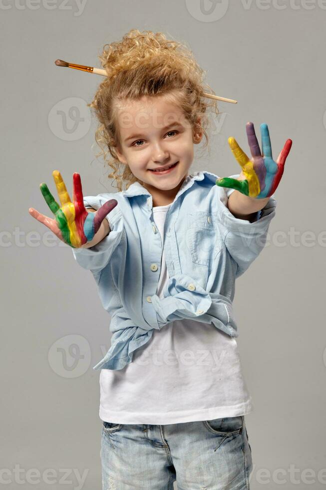 lindo pequeno menina com uma pintado mãos é posando em uma cinzento fundo. foto