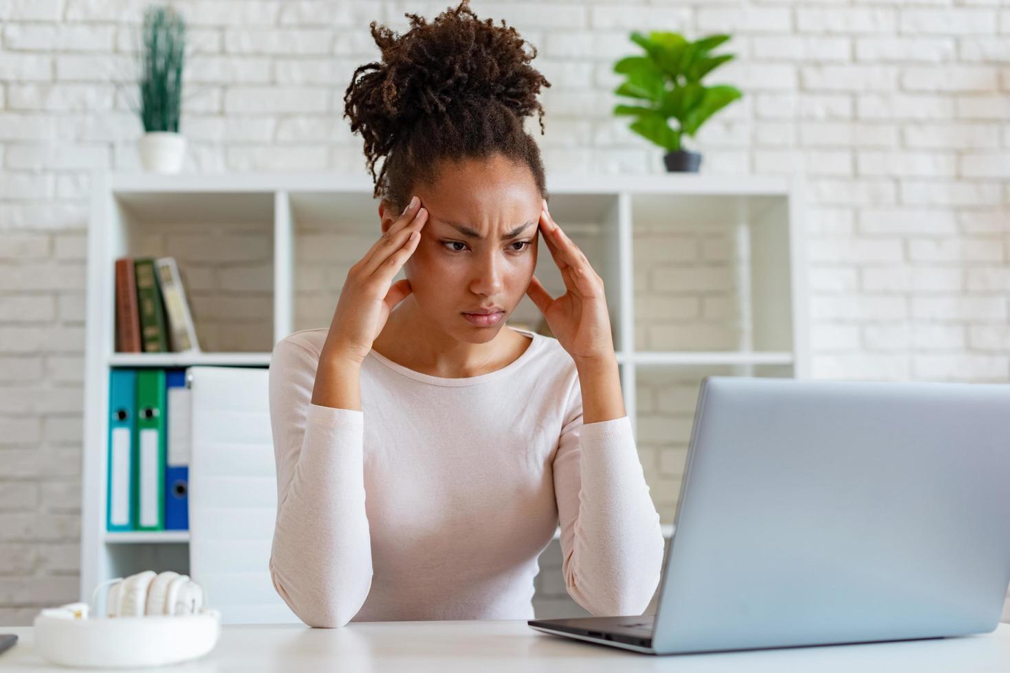 mulher tem uma dor de cabeça crônica, tocando as têmporas para aliviar a dor durante o trabalho no laptop foto