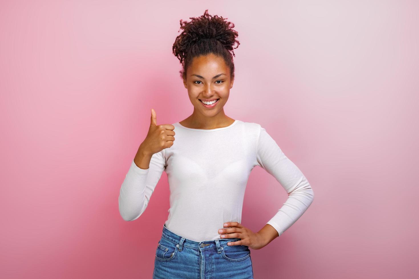 jovem mulata feliz em pé com os polegares para cima sobre um fundo rosa. foto