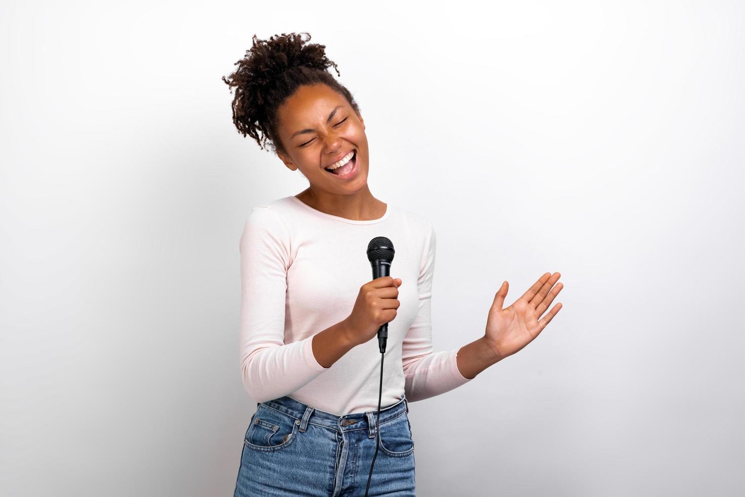 cantora mulata engraçada segurando um microfone nas mãos contra um fundo de estúdio de luz foto