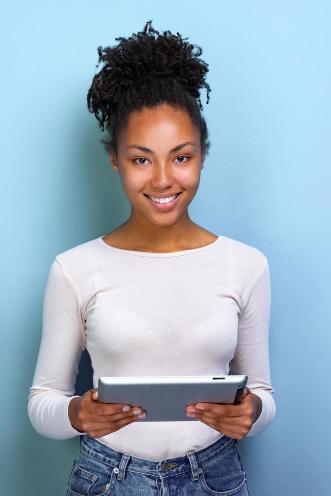 mulata feliz em pé com ipad olhando para a câmera e sorrindo alegremente. foto