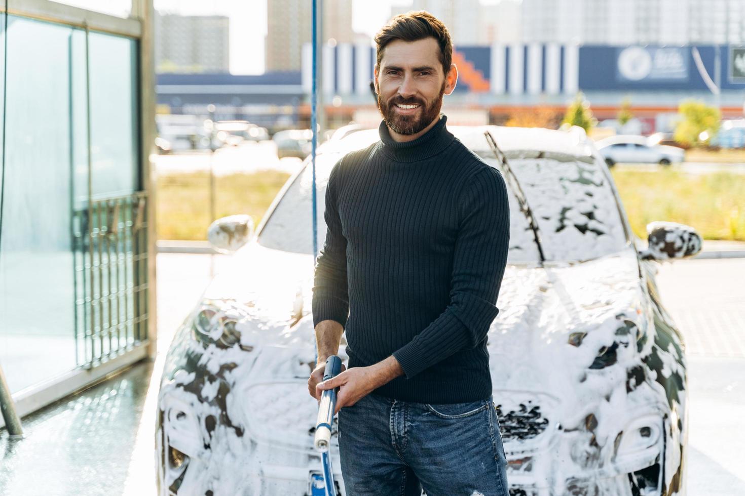 lavagem de carros. limpar o carro com água de alta pressão. lavagem de carro no lugar especial sozinho. homem sorrindo para a câmera enquanto lava o carro preto foto