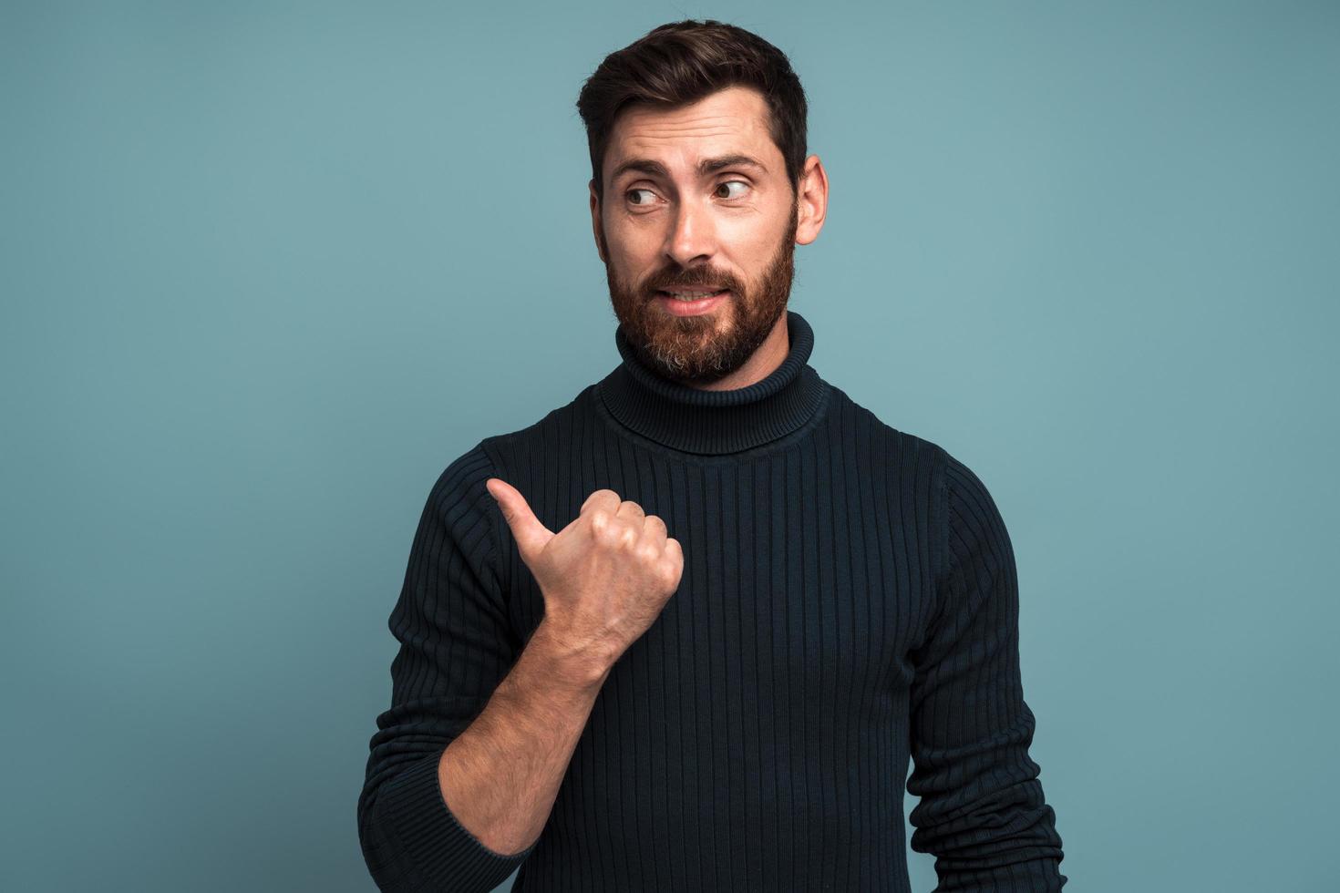 retrato de homem feliz e animado com barba apontando para o lado com o dedo, descubra a solução ou ideia, obter a resposta em questão, eureka. estúdio interno tiro isolado em fundo azul foto