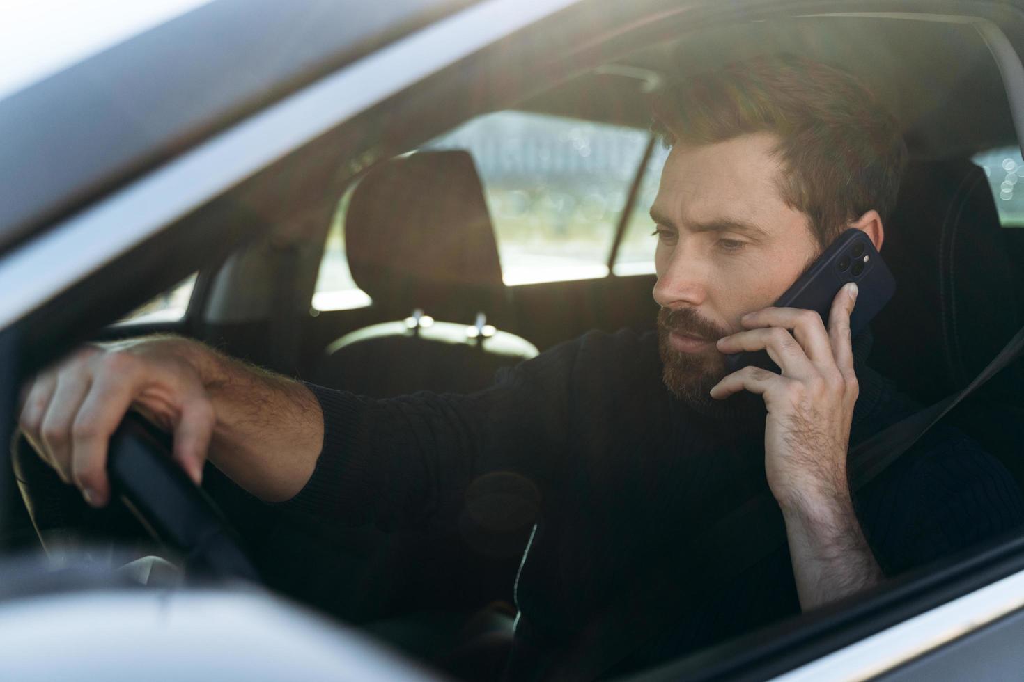 vista da rua para o homem caucasiano concentrado olhando para a janela enquanto conversa via smartphone com seu colega durante o longo caminho para o trabalho foto