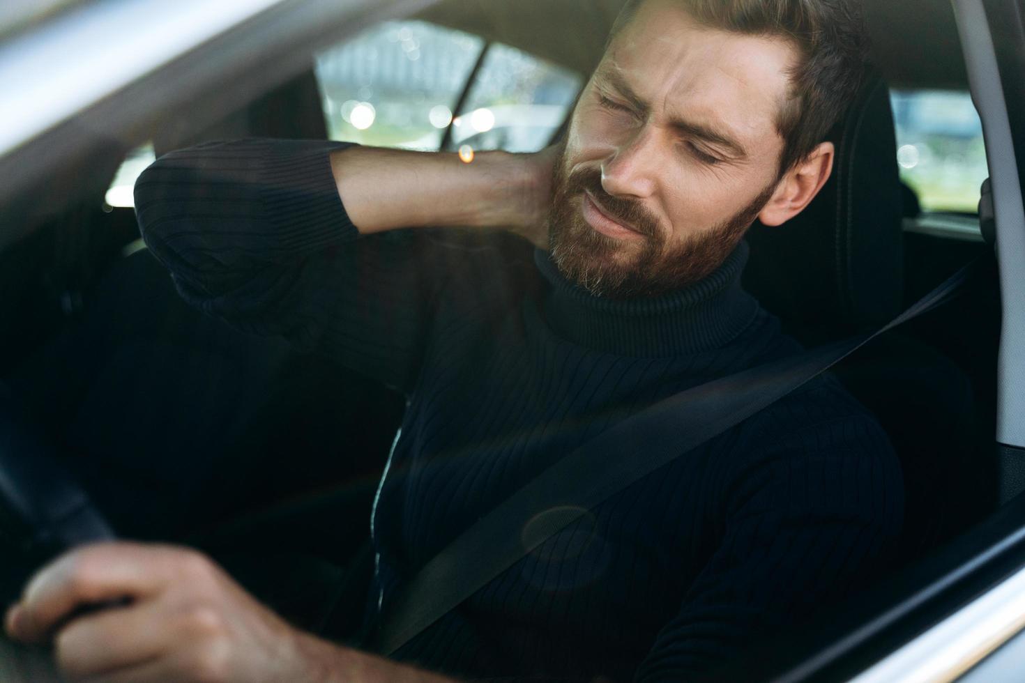 Estou cansado. vista da rua do jovem esfregando o pescoço dolorido, enquanto parecia cansado de dirigir. motorista do sexo masculino com dor de garganta, sentado em seu carro foto