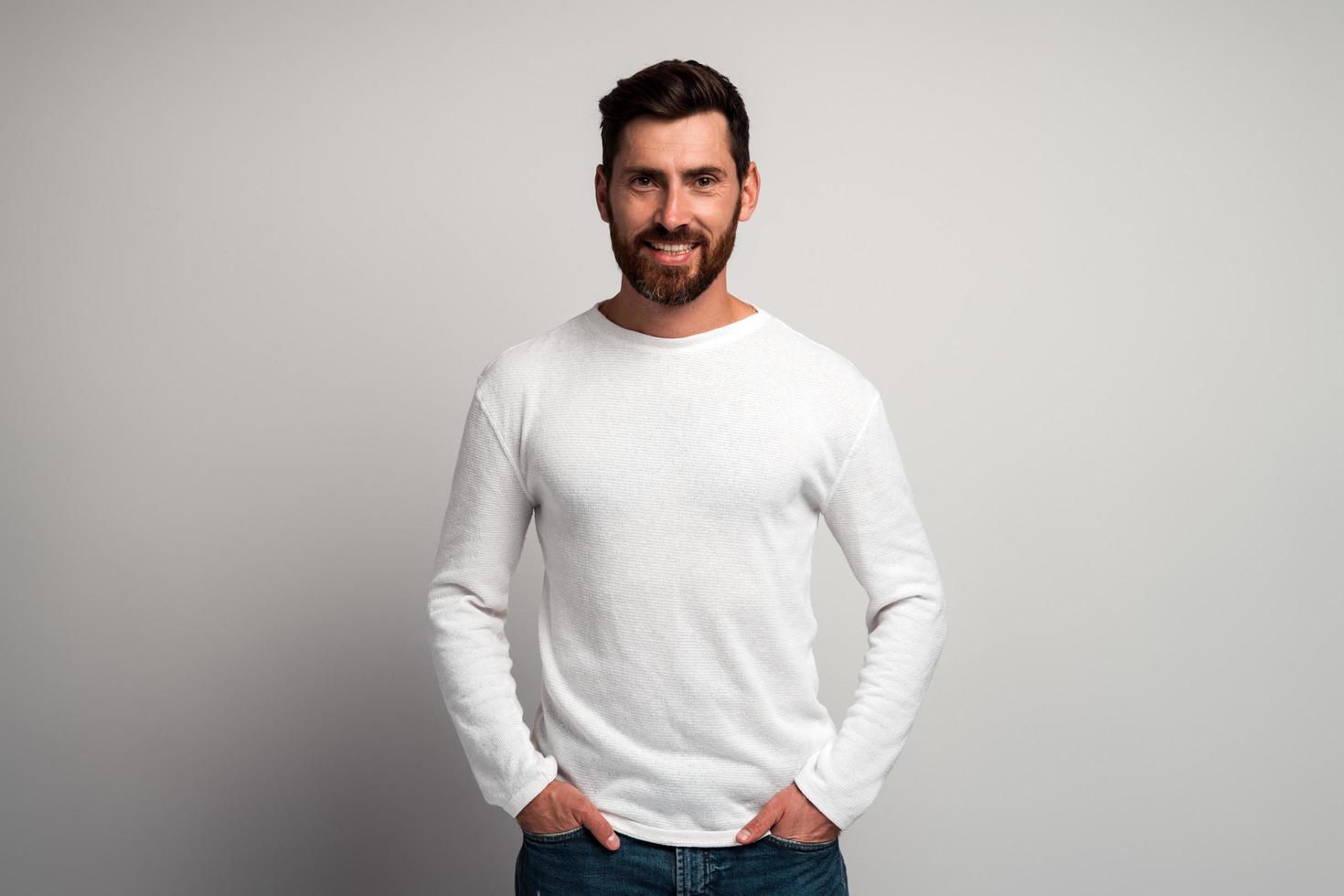 retrato de homem barbudo sorridente feliz com camisa branca contra um fundo cinza claro e sorrindo para a câmera. tiro do estúdio. conceito de emoções de pessoas foto