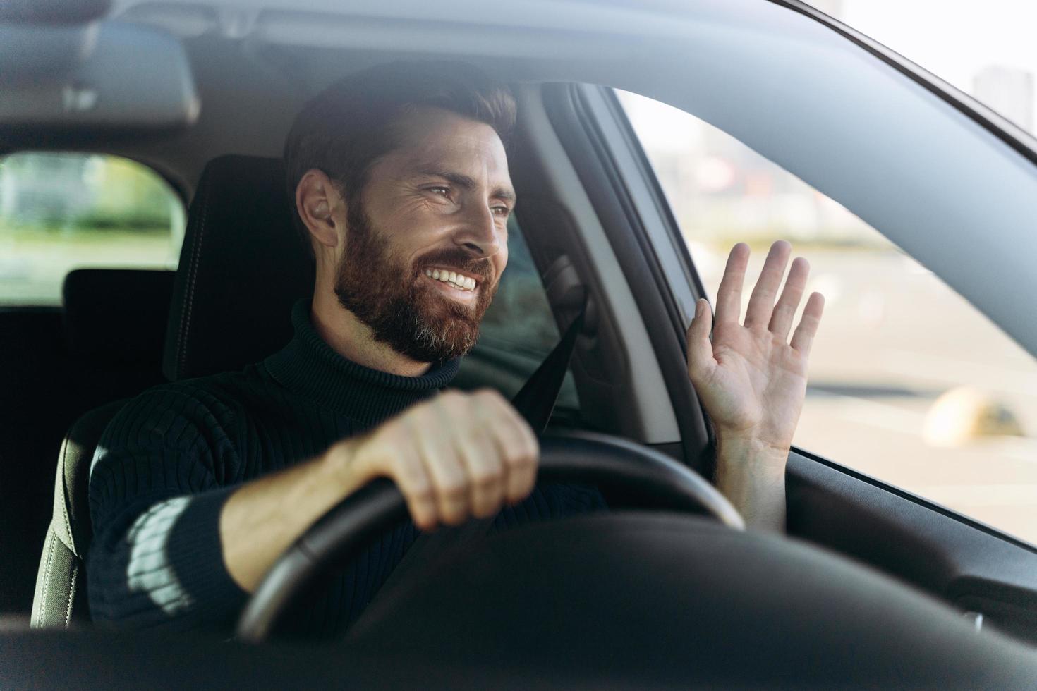 bonito jovem sorridente motorista de carro acenando com a mão como um sinal de saudação enquanto dirige o carro com emoções de prazer. conceito de transporte foto