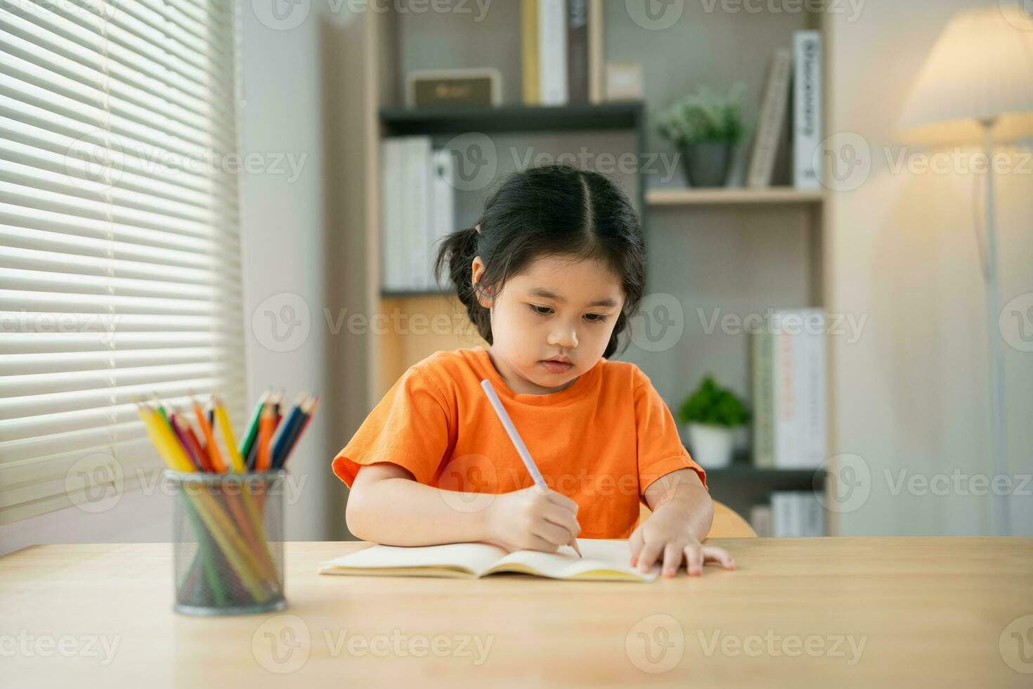 ásia bebê menina criança sorridente concentrado escrevendo desenhando colori lápis em Nota livro estude conectados em madeira mesa escrivaninha dentro vivo quarto às lar. Educação Aprendendo conectados a partir de casa conceito. foto