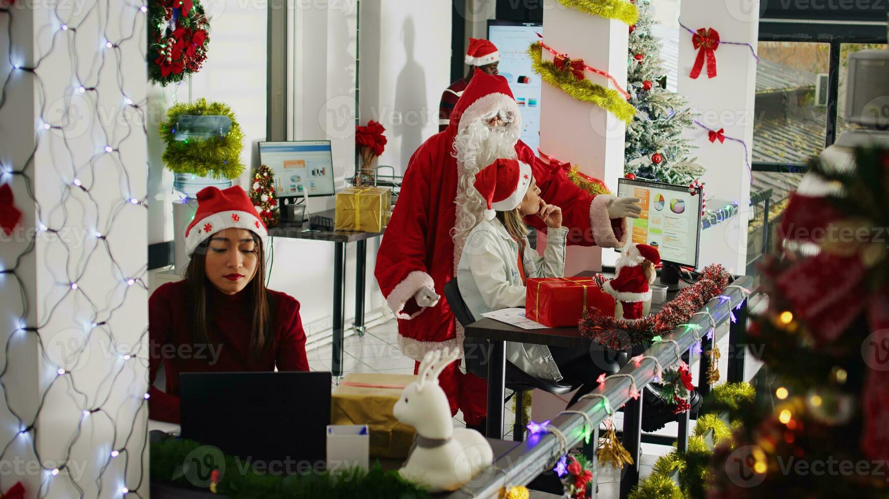 Gerente vestido Como santa dentro natal ornamentado escritório supervisionar tarefas depois de oferta apresenta para funcionários membros. equipe líder dentro festivo área de trabalho vestindo Natal traje examinando trabalhos feito de empregados foto