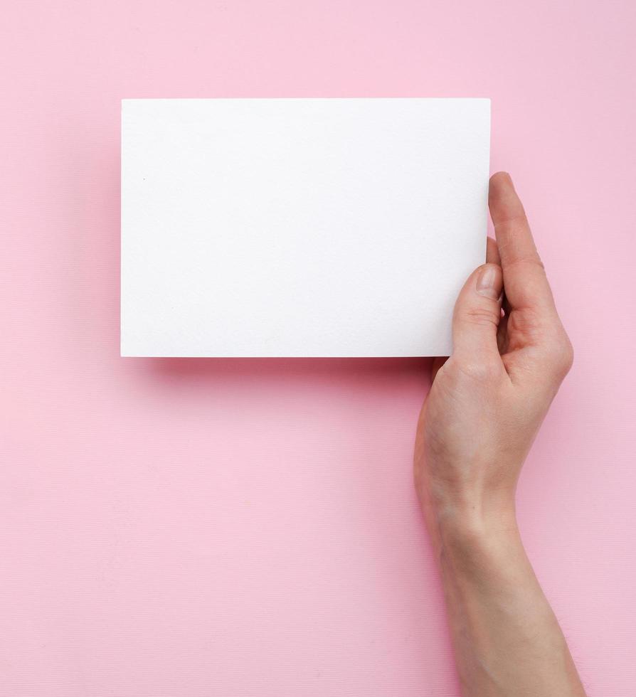 mão feminina segurando uma maquete de modelo vazio em branco em branco sobre um fundo rosa foto