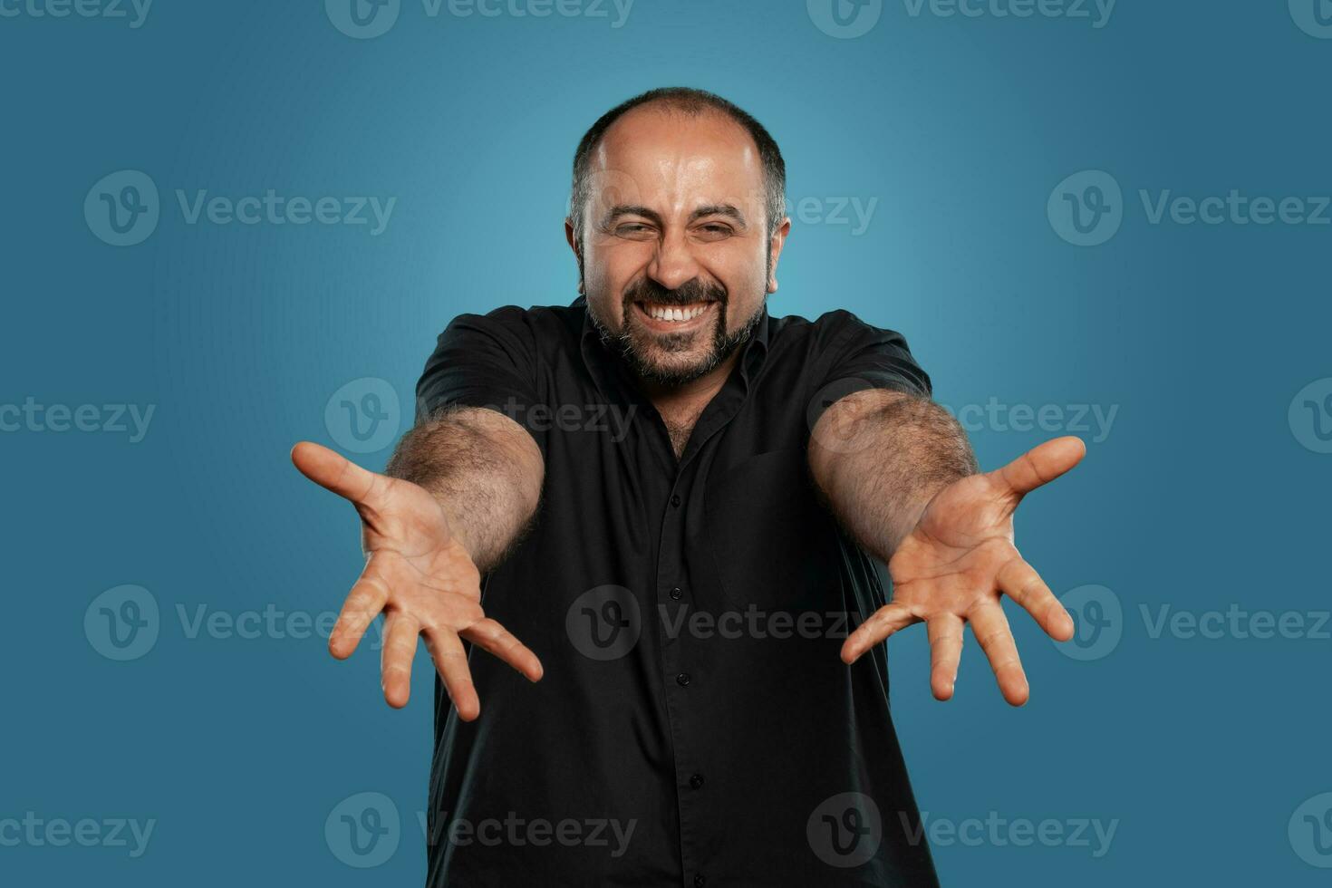 fechar-se retrato do uma moreno meia idade homem com barba, vestido dentro uma Preto camiseta e posando contra uma azul fundo. foto