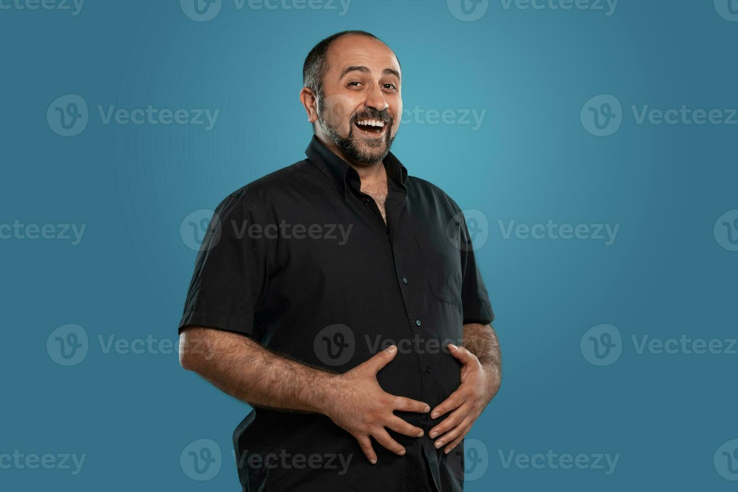 fechar-se retrato do uma moreno meia idade homem com barba, vestido dentro uma Preto camiseta e posando contra uma azul fundo. foto